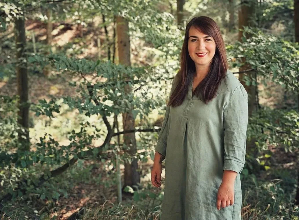 Sandra Fabri im Wald, in einem grünen Leinenkleid zwischen Buchen
